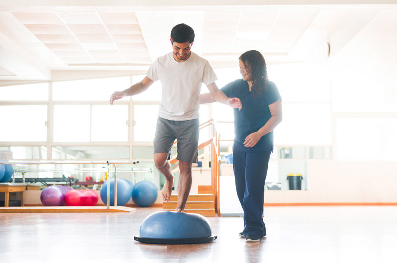 Male-patient-standing-on-bosu-ball-for-balance-improvement-and-fall-prevention-physical-therapy